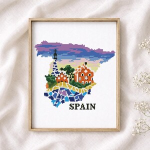Puede incluir: Arte de punto de cruz del mapa de Espa&ntilde;a, con arquitectura ic&oacute;nica en colores vibrantes. La obra est&aacute; enmarcada en un marco de madera clara e incluye la palabra "SPAIN". El fondo es una tela blanca suave.