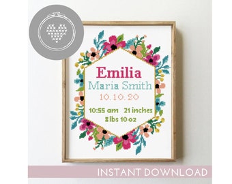 May include: A cross-stitch pattern featuring a floral wreath with a hexagonal frame. The frame contains the text "Emilia Maria Smith 10.10.20 10:55 am 21 inches 8 lbs 10 oz".