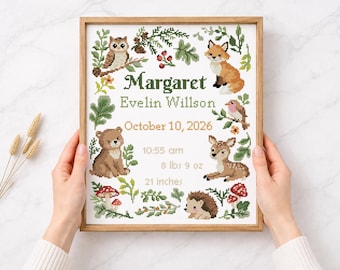 May include: A framed cross-stitch birth announcement featuring woodland animals and the name "Margaret Evelin Willson". The announcement includes the birth date, time, weight (8 lbs 9 oz), and length (21 inches). The frame is wood.