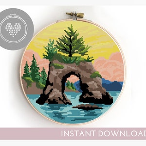 May include: Cross stitch pattern of a rock arch with a tree growing on top, surrounded by water and mountains in the background. The colors are yellow, orange, blue, green, and brown.
