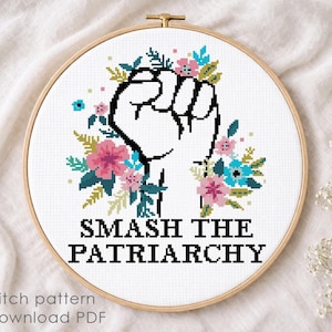 May include: A cross-stitch pattern in a wooden embroidery hoop featuring a raised fist outlined in black, surrounded by pink and blue flowers and green leaves. Below the design, the text reads SMASH THE PATRIARCHY in bold black capital letters.