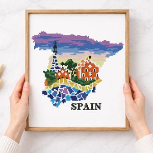 Puede incluir: Una obra de arte en punto de cruz enmarcada que representa el mapa de Espa&ntilde;a, con ilustraciones pixeladas de monumentos y un cielo colorido. La palabra "SPAIN" est&aacute; bordada en letras negras en la parte inferior.