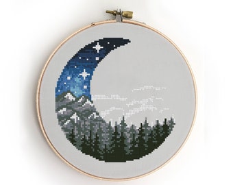 May include: Cross-stitch pattern of a crescent moon with a dark blue and white starry sky, mountains, and a forest of dark green trees. The pattern is framed in a wooden hoop.