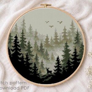 May include: A cross-stitch pattern of a forest scene, featuring dark green and black trees, a deer, and birds against a misty background. The design is framed in a wooden hoop. The text "Cross stitch pattern Instant download PDF" is visible.