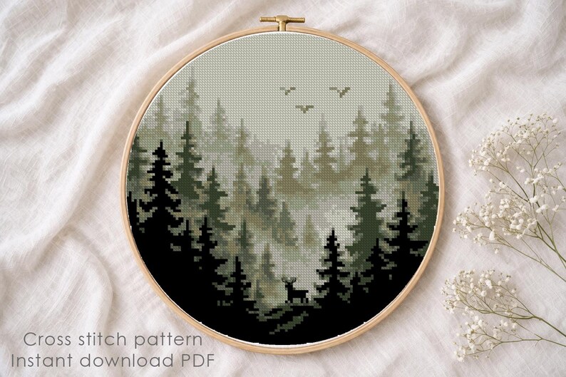 May include: A cross-stitch pattern of a forest scene, featuring dark green and black trees, a deer, and birds against a misty background. The design is framed in a wooden hoop. The text "Cross stitch pattern Instant download PDF" is visible.