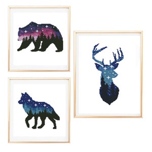 Op de afbeelding: Drie ingelijste prints met silhouetten van een beer, een hert en een wolf. Elk silhouet is gevuld met een sterrenhemel en een bos scène.