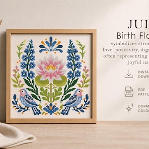 May include: A framed cross-stitch pattern featuring July birth flowers. The design includes a pink water lily, blue flowers, green leaves, and two birds. The text reads "JULY Birth Flowers" and mentions "Instant Download" and "Dopamine Colors."