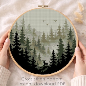 May include: A cross-stitch pattern of a forest scene in a wooden hoop. The design features dark green and black trees, a deer, and birds against a misty background. The text "Cross stitch pattern Instant download PDF" is visible.