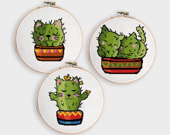 May include: Three embroidery patterns featuring cute cats in cactus pots. The first pattern shows a single cat sleeping in a green cactus pot with a red, yellow, and orange patterned design. The second pattern shows two cats cuddling in a green cactus pot with a red, yellow, and green patterned design. The third pattern shows a single cat standing in a green cactus pot with a red, yellow, and blue patterned design.