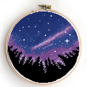 Può includere: Ricamo a punto croce in un telaio di legno raffigurante una scena del cielo notturno. Il disegno presenta un cielo blu scuro con stelle bianche, una nebulosa viola e rosa e una silhouette nera di una foresta. Artigianato fatto a mano.