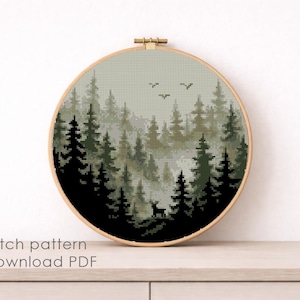 May include: A cross-stitch pattern of a forest scene in a round wooden hoop. The design features dark green and black trees, a deer, and birds against a misty background. The text "Cross stitch pattern Instant download PDF" is at the bottom.