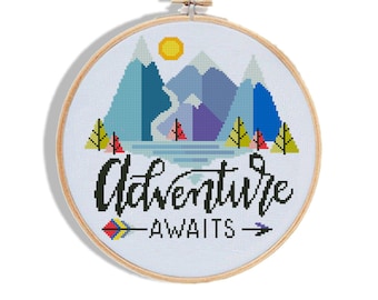May include: Cross stitch pattern featuring a mountain range with a lake and the text "Adventure Awaits" with an arrow. The mountains are blue, purple, and green. The lake is blue and the arrow is red, yellow, and blue.