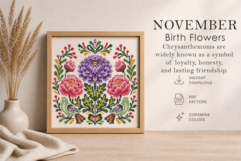 May include: A framed cross-stitch pattern featuring a floral design with a central purple flower and two pink flowers. The text "NOVEMBER Birth Flowers" is at the top, with additional text below. The design includes green leaves and birds.