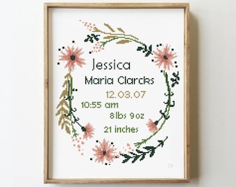 May include: A framed cross-stitch with a floral wreath design. The wreath is made of pink flowers, green leaves, and gold stems. The center of the wreath includes the name "Jessica Maria Clarks", the date "12.03.07", the time "10:55 am", the weight "8 lbs 9 oz", and the length "21 inches".