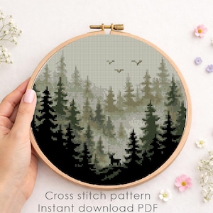 May include: A cross-stitch pattern of a forest scene in a wooden embroidery hoop. The design features dark green trees, a deer, and birds against a misty background. The text "Cross stitch pattern Instant download PDF" is visible.