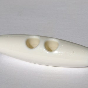 May include: White plastic button with two holes. The button is oval shaped and has a smooth surface.