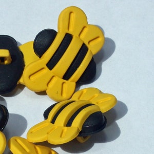 May include: Five yellow and black bee-shaped buttons with a black center. The buttons are about the size of a US quarter.