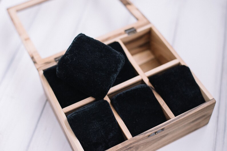 May include: A wooden watch box with a glass lid, containing six black velvet watch cushions.