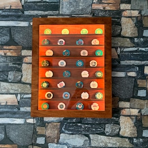 Op de afbeelding: Een houten display met meerdere planken, met een verzameling kleurrijke pokerchips. De kast heeft een donkerbruine lijst en een heldere voorkant, met de chips netjes gerangschikt. De achtergrond is een stenen muur.