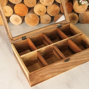 May include: A wooden box with a glass lid and eight compartments. The box is made of light brown wood and has a natural finish. The lid is hinged and has a brass latch.