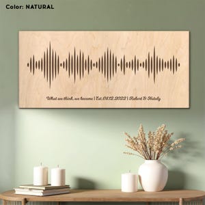Può includere: Un'opera d'arte a onde sonore in legno naturale con il testo "What we think, we become | Est. 08.12.2022 | Robert & Nataly" inciso su di essa.
