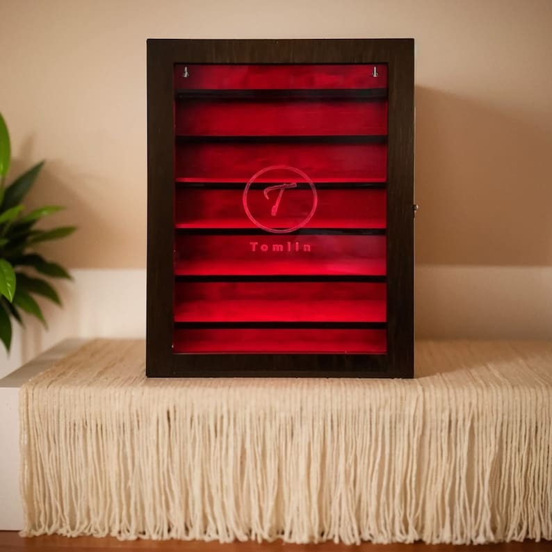 May include: A dark wood display case with a red glass interior and eight shelves. The case has a logo with the letter "T" and the word "Tomlin" etched into the glass.