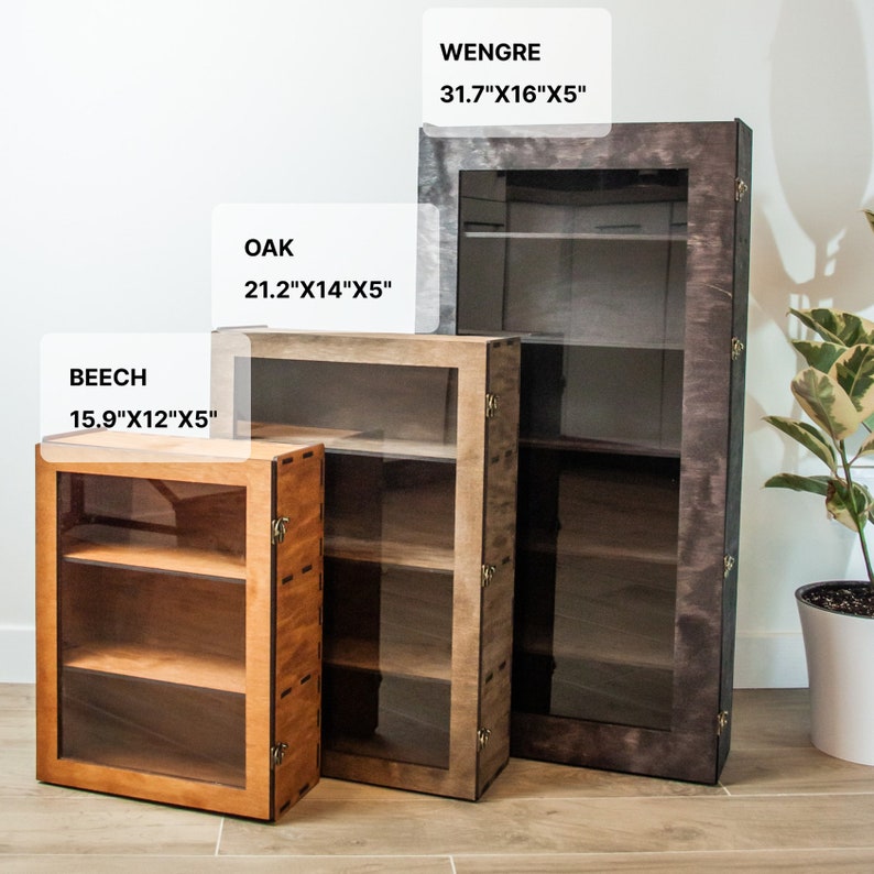 May include: Three wooden display cabinets with glass doors and shelves. The cabinets are in different sizes and wood finishes: beech, oak, and wengre. The beech cabinet is 15.9 inches wide by 12 inches deep by 5 inches tall. The oak cabinet is 21.2 inches wide by 14 inches deep by 5 inches tall. The wengre cabinet is 31.7 inches wide by 16 inches deep by 5 inches tall.