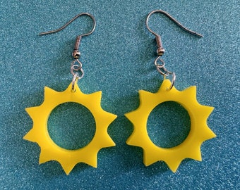 May include: A pair of yellow sun earrings with silver hooks. The earrings are shaped like a sun with a circle in the middle.