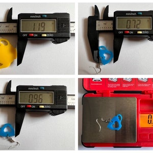 May include: Two pairs of earrings, one yellow and one blue, shaped like teacups. The earrings are measured with a caliper and weighed on a digital scale. The yellow earring measures 1.19 inches and the blue earring measures 0.96 inches. The blue earring weighs 0.30 ounces.