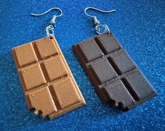 May include: A pair of chocolate bar earrings. One earring is brown and the other is a lighter brown. Both earrings have a bite taken out of them.