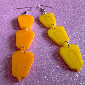 May include: A pair of dangle earrings with three yellow and orange teardrop-shaped charms on each earring.