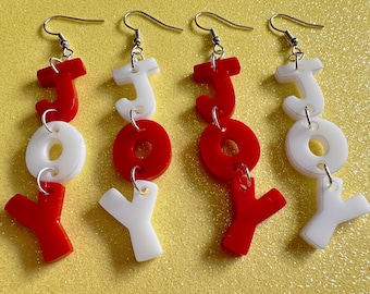 May include: A pair of red and white acrylic earrings spelling out the word "JOY". Each earring has three letters, with the "J" at the top and the "Y" at the bottom. The letters are connected by a small silver ring.