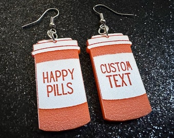 May include: A pair of orange pill bottle earrings. One earring says "HAPPY PILLS" and the other says "CUSTOM TEXT".