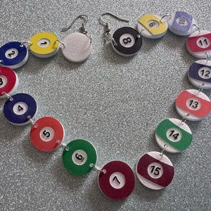 May include: A necklace made of white, red, blue, green, and yellow painted wooden circles. Each circle has a black number on it, from 1 to 15. The necklace is in the shape of a heart.