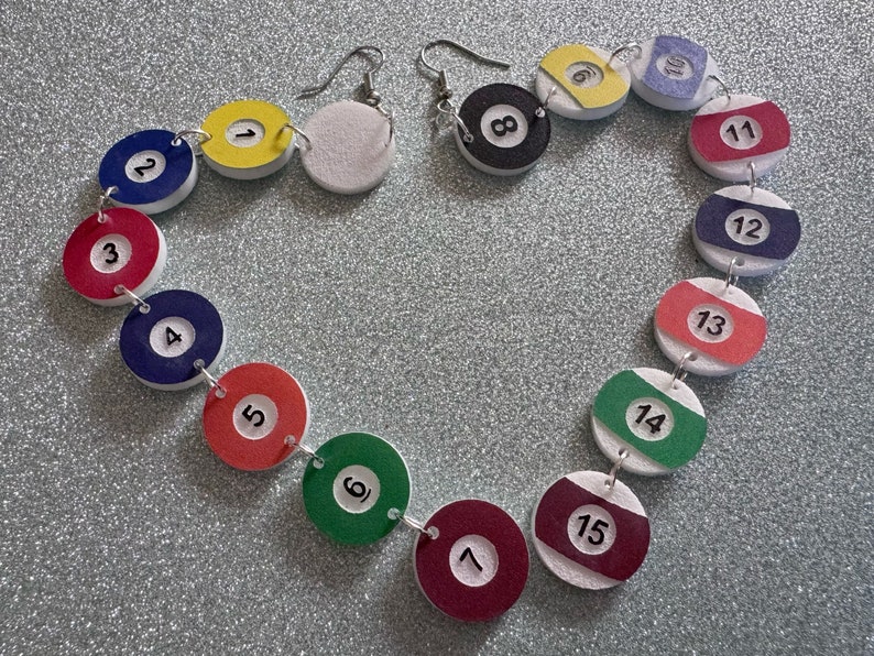 May include: A necklace made of white, red, blue, green, and yellow painted wooden circles. Each circle has a black number on it, from 1 to 15. The necklace is in the shape of a heart.