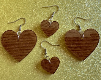 May include: Three pairs of wooden heart-shaped earrings with silver hooks. The hearts are a dark brown color with a wood grain pattern.