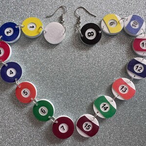 May include: A pair of earrings with white and black billiard ball charms. The charms are numbered 1 through 15 and are connected by silver jump rings. The earrings are hanging from silver hooks.