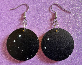 May include: A pair of black circle earrings with white stars and a silver hook.