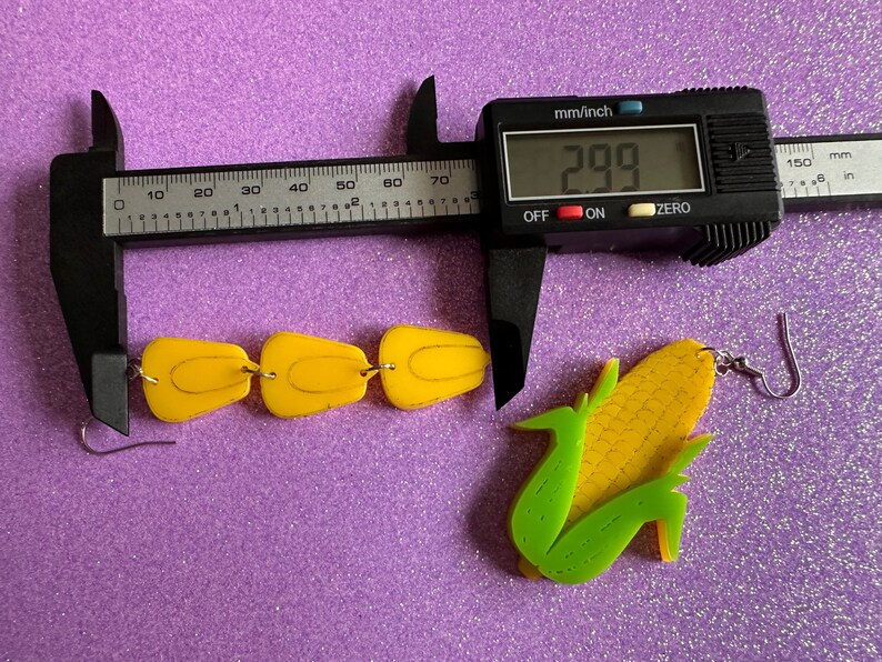 May include: A pair of yellow and green corn on the cob earrings. The earrings are made of acrylic and measure 2.99 inches in length.