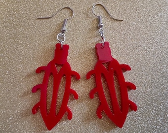 May include: A pair of red acrylic earrings shaped like a stylized insect with silver hooks.