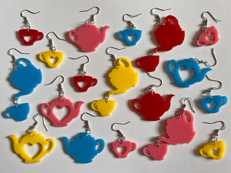 May include: Assortment of colorful acrylic earrings featuring teapots and teacups with heart cutouts. The earrings are available in pink, red, yellow, blue, and teal.