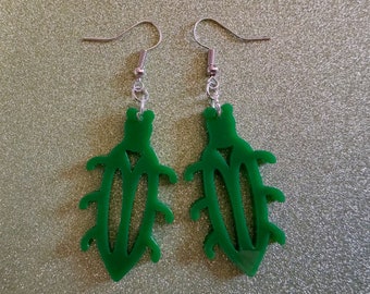 May include: A pair of green acrylic earrings shaped like stylized beetles. The earrings have silver hooks.