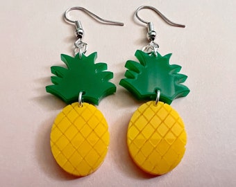 May include: A pair of pineapple earrings with green tops and yellow bottoms. The earrings are made of acrylic and have silver hooks.