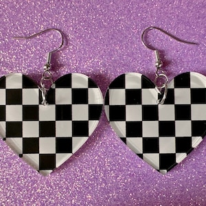 May include: A pair of heart-shaped earrings with a black and white checkered pattern. The earrings are made of clear acrylic and have silver hooks.