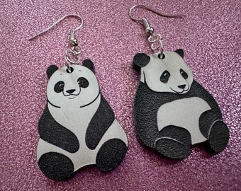 May include: A pair of dangle earrings featuring black and white panda bear charms. The earrings are made of wood and have silver hooks.