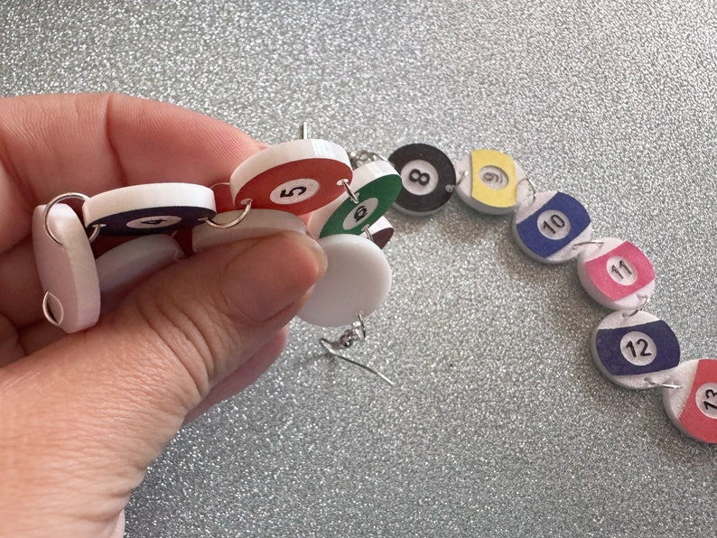 May include: A colorful necklace made of round, white, red, green, yellow, blue, and pink plastic beads with black numbers 5, 8, 10, 11, 12, and 13 printed on them.