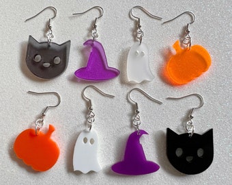 May include: Six pairs of Halloween-themed earrings. The earrings are made of acrylic and feature a variety of designs, including a black cat, a purple witch hat, a white ghost, and an orange pumpkin. The earrings are all on silver hooks.