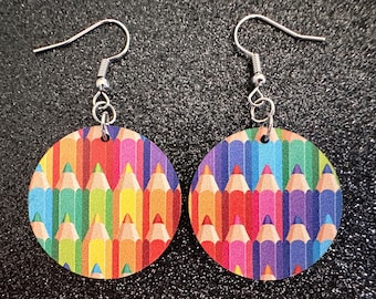 May include: A pair of earrings featuring a colorful pattern of pencils. The earrings are round and have silver hooks.