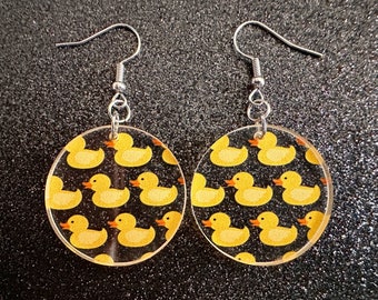 May include: A pair of silver earrings with round clear acrylic charms featuring a repeating pattern of yellow rubber duckies.