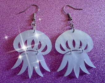 May include: A pair of white iridescent acrylic earrings shaped like jellyfish. The earrings have a silver hook and a silver jump ring.